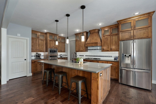 kitchen featuring decorative light fixtures, stainless steel appliances, sink, premium range hood, and a center island with sink