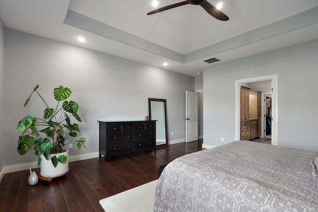 bedroom with ceiling fan, dark wood-type flooring, connected bathroom, and a tray ceiling