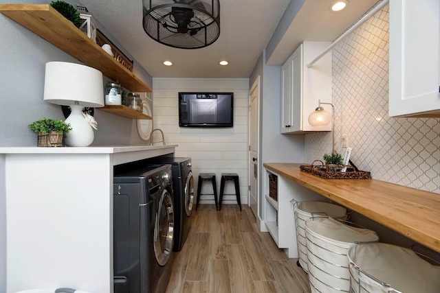 clothes washing area with wood walls, washer and clothes dryer, and light wood-type flooring