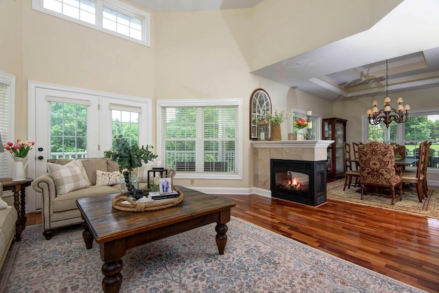 living room featuring a tile fireplace, a towering ceiling, dark hardwood / wood-style flooring, a notable chandelier, and a raised ceiling