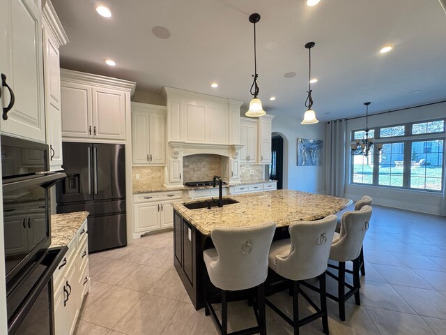 kitchen featuring black appliances, tasteful backsplash, white cabinets, light stone counters, and a center island with sink