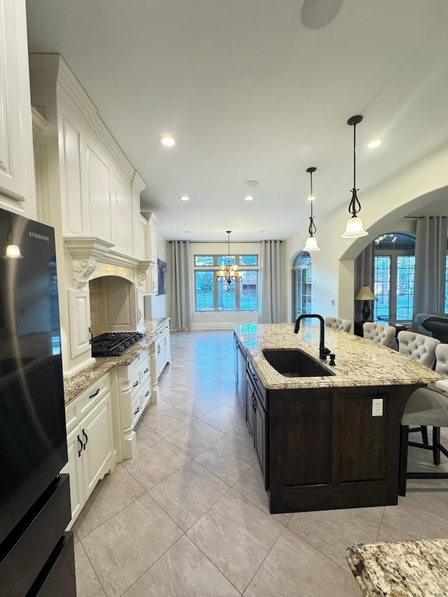 kitchen with pendant lighting, white cabinetry, an island with sink, sink, and black fridge