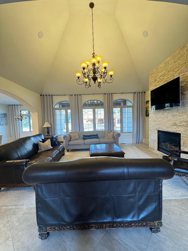 living room featuring an inviting chandelier, high vaulted ceiling, and a stone fireplace