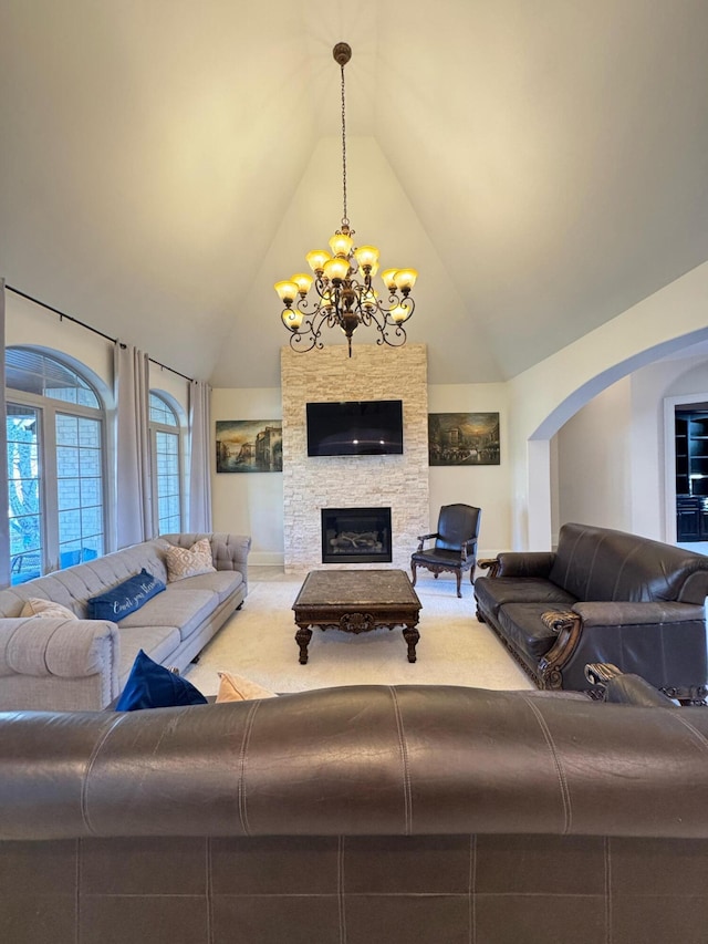 carpeted living room with a chandelier, high vaulted ceiling, and a stone fireplace