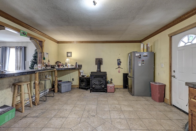 kitchen featuring crown molding, a textured ceiling, a wood stove, and stainless steel refrigerator