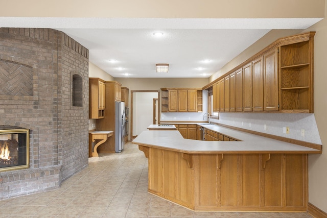 kitchen featuring a kitchen bar, sink, stainless steel refrigerator, kitchen peninsula, and a fireplace