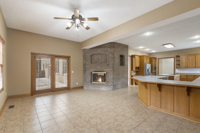 kitchen with stainless steel fridge, a kitchen bar, kitchen peninsula, a brick fireplace, and a textured ceiling