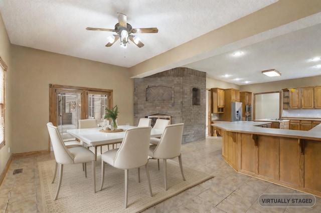 dining area with ceiling fan, a textured ceiling, a brick fireplace, and light tile patterned floors