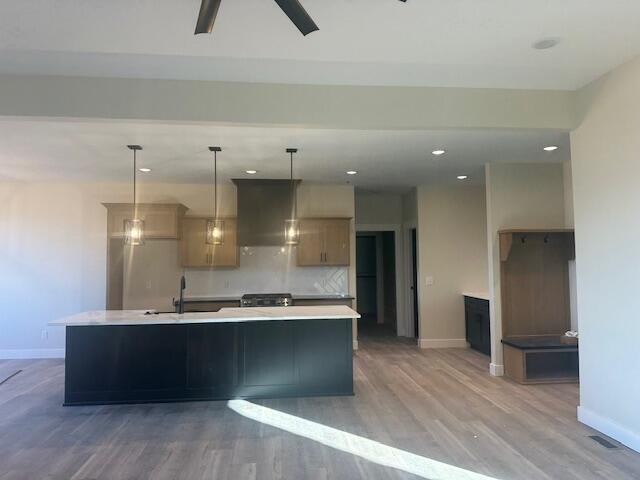 kitchen with pendant lighting, sink, wall chimney exhaust hood, tasteful backsplash, and a kitchen island with sink