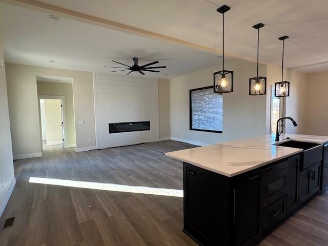 kitchen featuring dark wood-type flooring, sink, hanging light fixtures, a large fireplace, and a kitchen island with sink