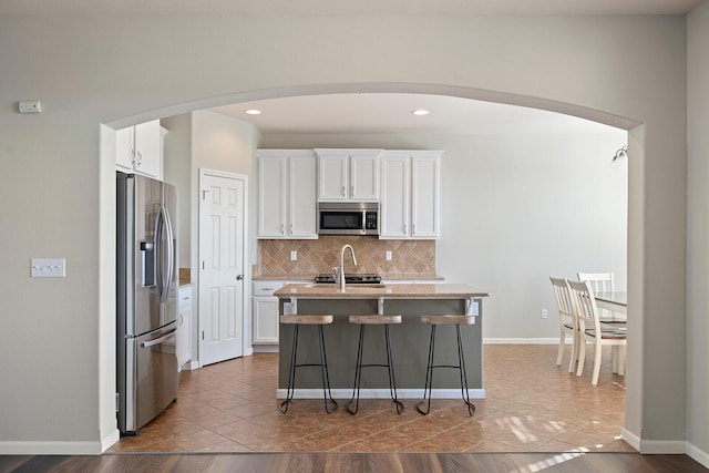 kitchen featuring appliances with stainless steel finishes, white cabinetry, decorative backsplash, an island with sink, and a breakfast bar area