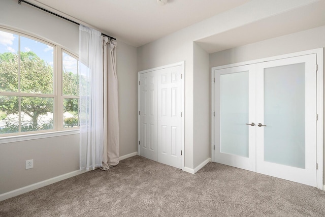 unfurnished bedroom with multiple windows, light colored carpet, and french doors