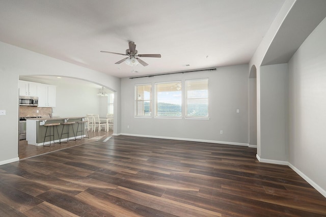 unfurnished living room featuring ceiling fan with notable chandelier and dark hardwood / wood-style floors