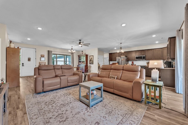 living room with ceiling fan with notable chandelier and light hardwood / wood-style floors