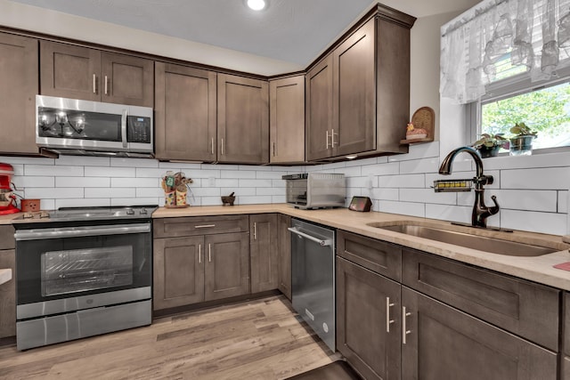 kitchen with appliances with stainless steel finishes, decorative backsplash, sink, light wood-type flooring, and dark brown cabinets