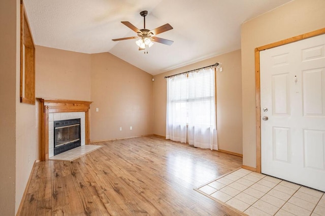 unfurnished living room with a tiled fireplace, ceiling fan, lofted ceiling, and light wood-type flooring