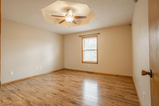 spare room with ceiling fan, a textured ceiling, light wood-type flooring, and a tray ceiling