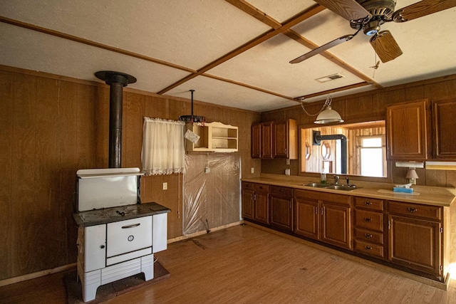 kitchen featuring hanging light fixtures, sink, a wood stove, ceiling fan, and wood walls