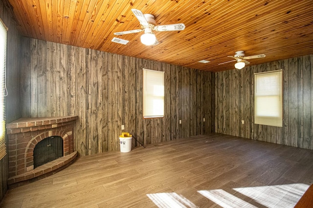 unfurnished living room featuring light wood-type flooring, ceiling fan, a brick fireplace, and wood walls