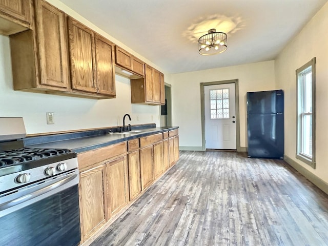 kitchen with sink, black refrigerator, an inviting chandelier, gas range, and light wood-type flooring