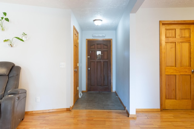 foyer featuring baseboards, light wood finished floors, and a textured ceiling