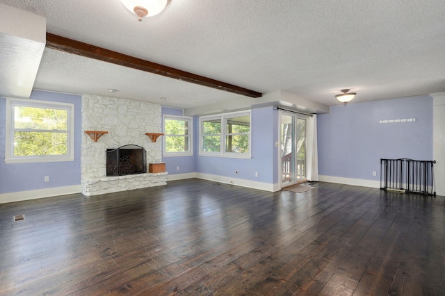 unfurnished living room featuring beam ceiling, a stone fireplace, dark wood-type flooring, and a wealth of natural light