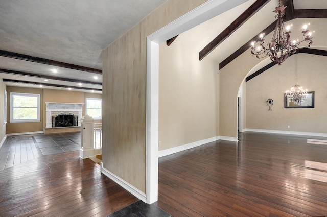 unfurnished living room with dark hardwood / wood-style flooring, vaulted ceiling with beams, a stone fireplace, and an inviting chandelier