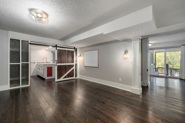 interior space with sink, decorative columns, a textured ceiling, dark hardwood / wood-style flooring, and a barn door