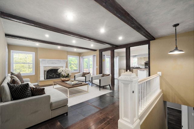 living room featuring dark wood-type flooring, a stone fireplace, beam ceiling, and a wealth of natural light