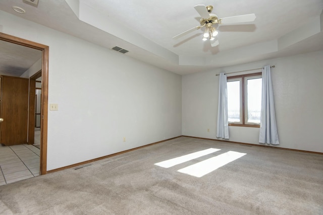 carpeted spare room with a raised ceiling and ceiling fan