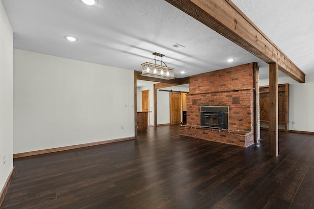 unfurnished living room with dark hardwood / wood-style flooring, a textured ceiling, a barn door, and beamed ceiling