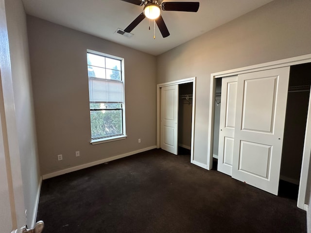 unfurnished bedroom featuring multiple closets, ceiling fan, and dark carpet