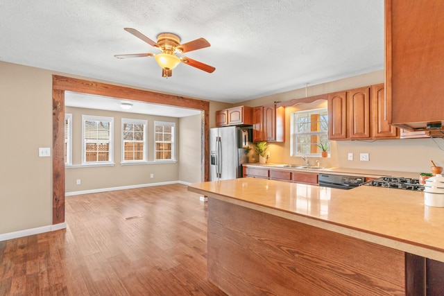 kitchen featuring ceiling fan, stainless steel fridge with ice dispenser, light countertops, a peninsula, and brown cabinetry