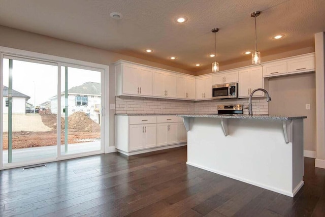 kitchen with a breakfast bar area, white cabinetry, light stone counters, appliances with stainless steel finishes, and pendant lighting