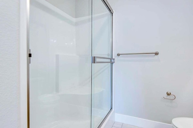 bathroom featuring a shower with door, tile patterned floors, and toilet