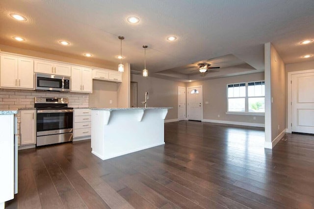 kitchen featuring a raised ceiling, white cabinets, decorative backsplash, hanging light fixtures, and stainless steel appliances