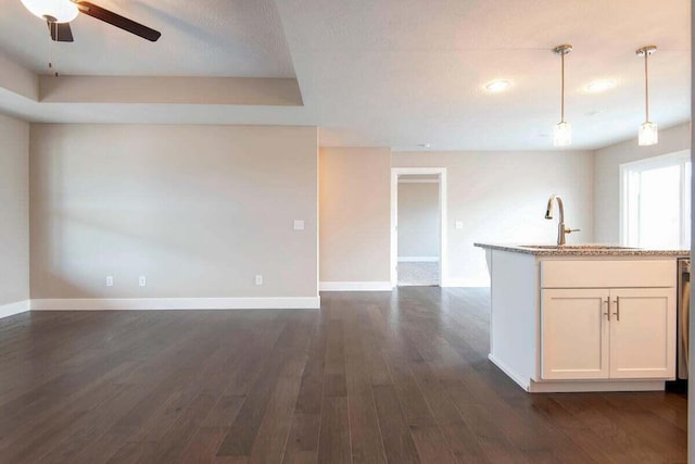 kitchen featuring white cabinetry, sink, hanging light fixtures, light stone counters, and dark wood-type flooring