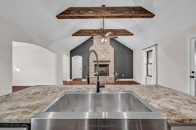 kitchen featuring a stone fireplace, sink, vaulted ceiling with beams, ceiling fan, and hardwood / wood-style floors