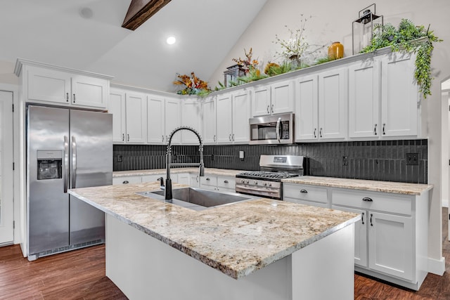 kitchen with sink, appliances with stainless steel finishes, an island with sink, white cabinets, and vaulted ceiling