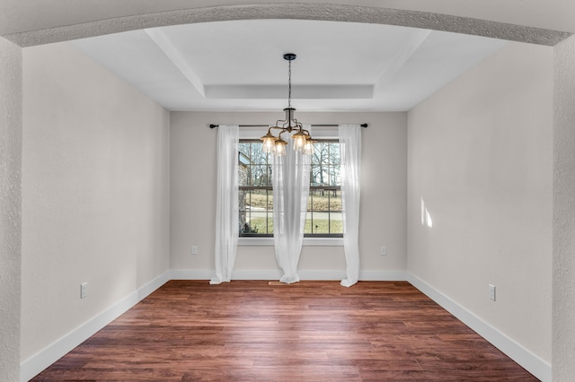 unfurnished dining area featuring an inviting chandelier, dark hardwood / wood-style floors, and a raised ceiling