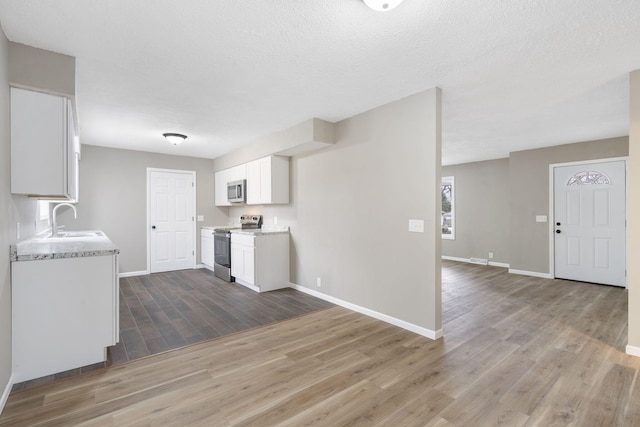 kitchen with appliances with stainless steel finishes, sink, white cabinets, light stone countertops, and a textured ceiling