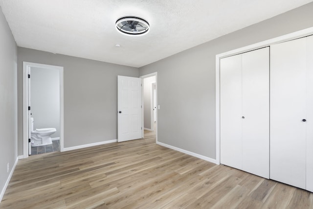 unfurnished bedroom featuring ensuite bathroom, a textured ceiling, a closet, and light wood-type flooring