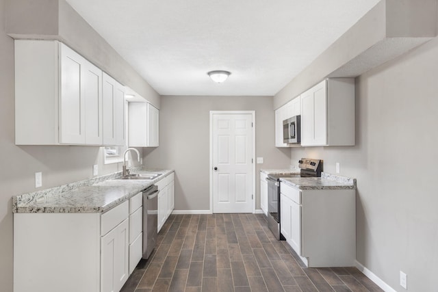 kitchen with stainless steel appliances, white cabinetry, light stone countertops, and sink