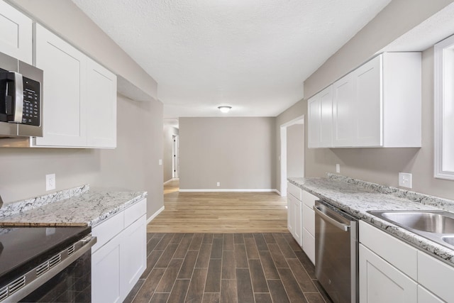 kitchen with stainless steel appliances, white cabinetry, and light stone counters