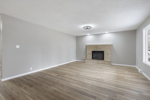 unfurnished living room with light wood-type flooring, a wealth of natural light, a textured ceiling, and a fireplace