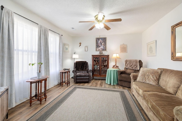 living room featuring ceiling fan, light hardwood / wood-style floors, and a textured ceiling