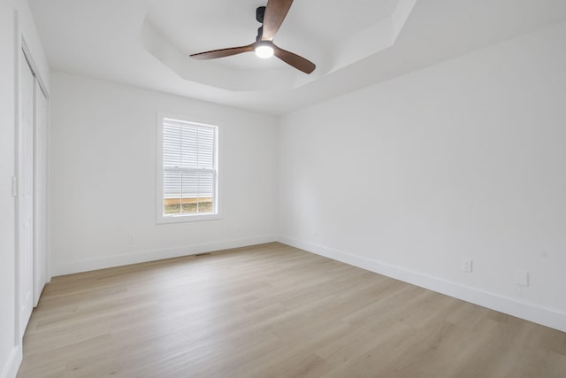 empty room featuring ceiling fan, a raised ceiling, and light wood-type flooring