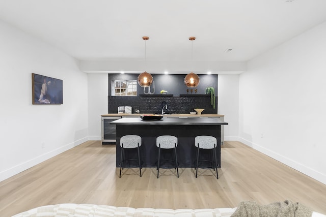 bar featuring decorative light fixtures, sink, wine cooler, backsplash, and light hardwood / wood-style floors