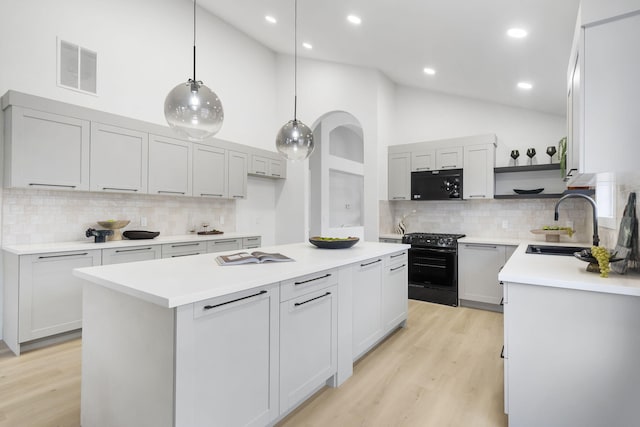 kitchen featuring sink, backsplash, hanging light fixtures, a center island, and gas range