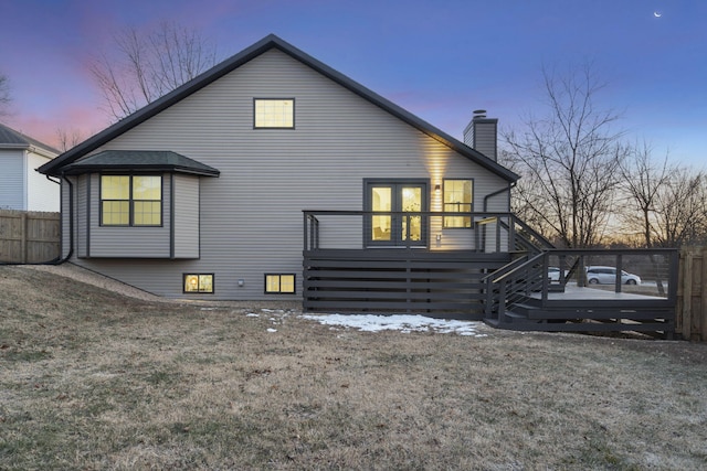 back house at dusk with a lawn and a deck